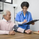 Infirmière en EHPAD prenant la tension d’un résident pour le suivi médical dans un logiciel de soins