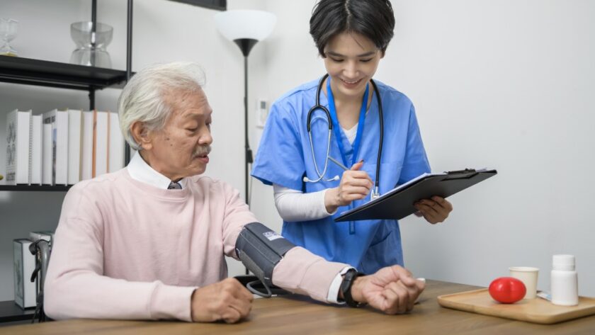 Infirmière en EHPAD prenant la tension d’un résident pour le suivi médical dans un logiciel de soins